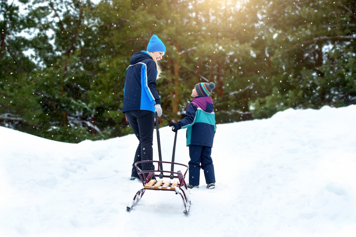 Un enfant en veste bleu et sa maman en veste en bleu sont en train de remonter la piste de luge.