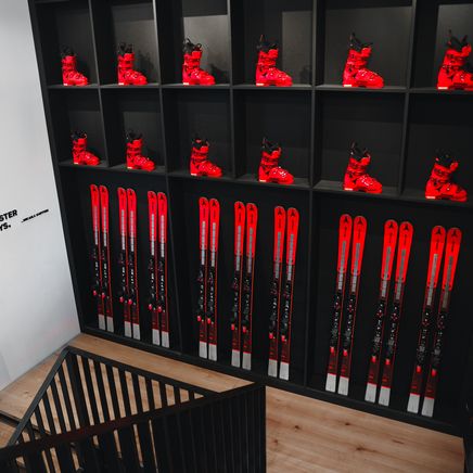 Mur noir présentant des skis et chaussures rouges. Un escalier en bois à gauche, avec une citation inspirante sur le mur blanc.