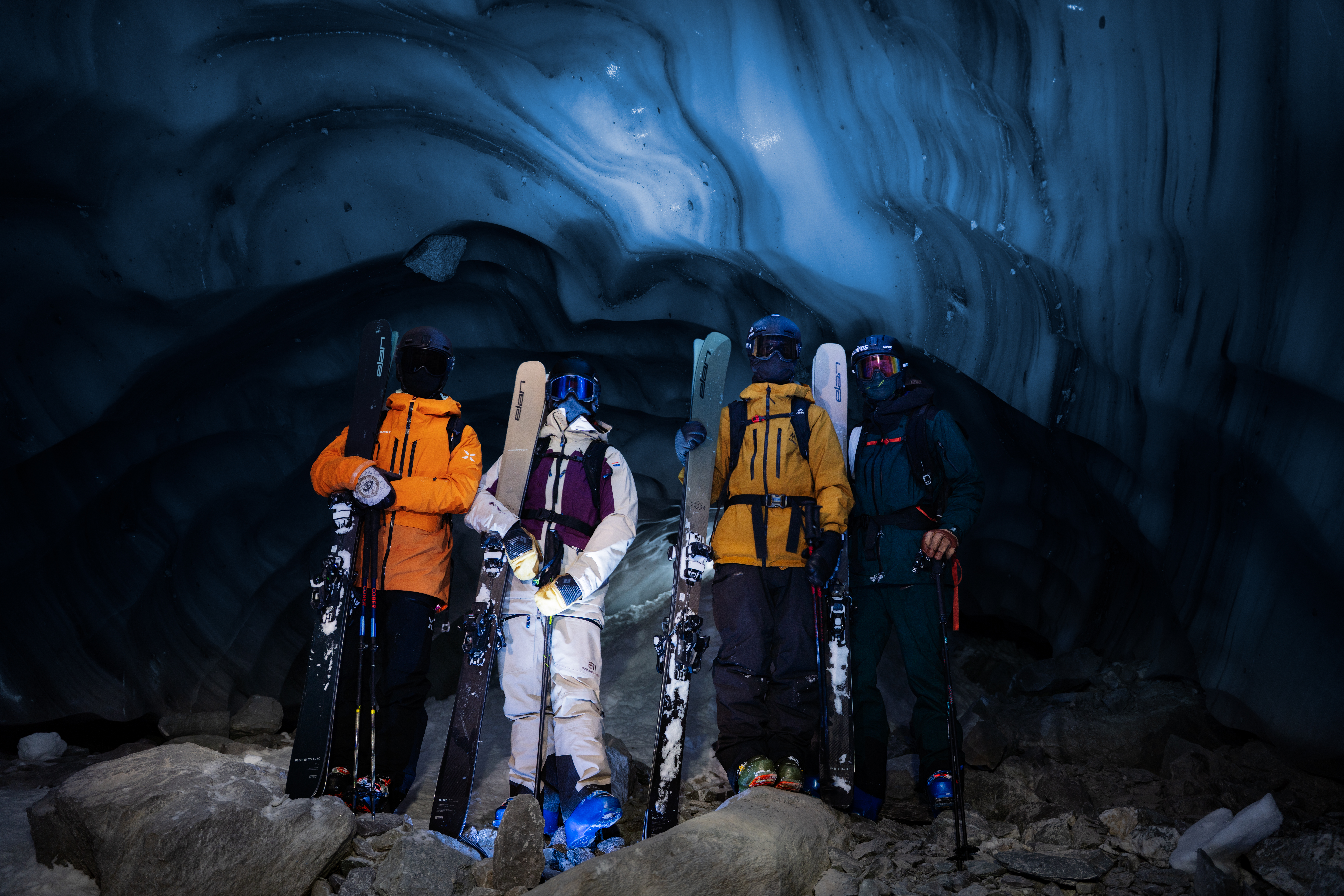 Quatre skieurs avec leurs skis posant dans une grotte de glace bleue aux murs sculptés.