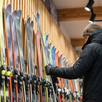 Un homme en doudoune et bonnet examine des skis colorés alignés dans un magasin de sport.