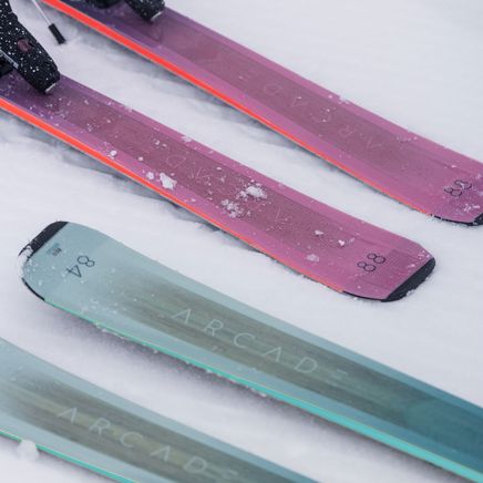 Deux paires de skis ARCADE posées sur la neige, une violette (88) et une vert-bleu (84), avec leurs fixations.